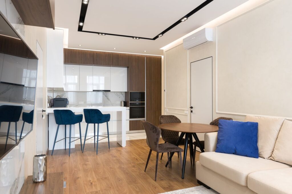 Comfortable sofa with cushions placed in front of TV in modern studio apartment with kitchen and dining zones