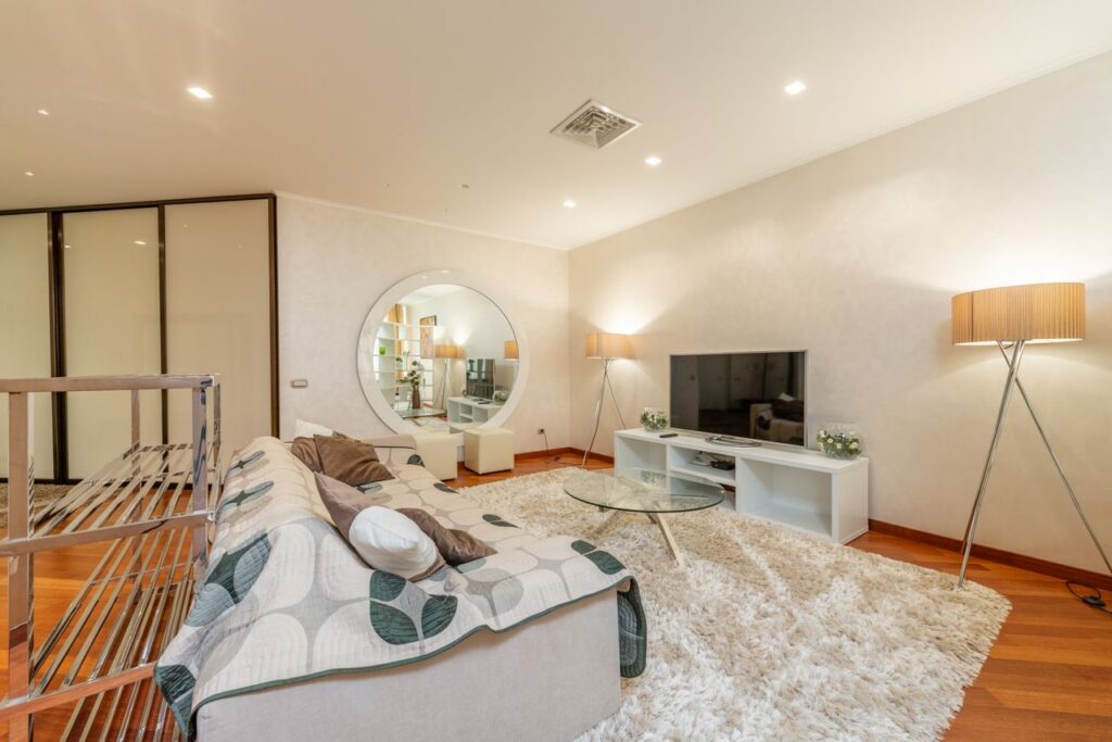 Comfortable sofa with small glass round coffee table placed on soft rug near modern TV in spacious illuminated living room